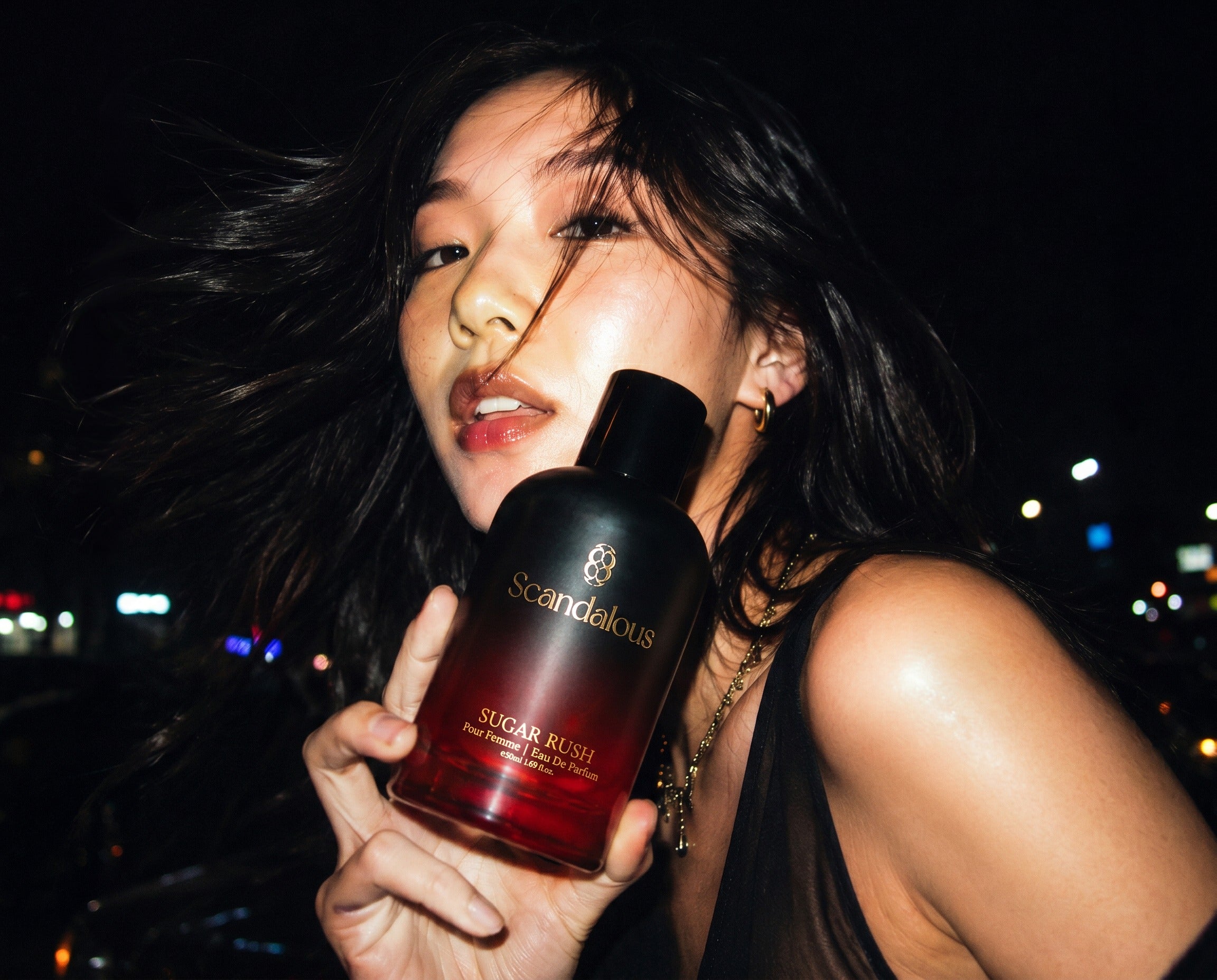 Model at night holding Scandalous Sugar Rush perfume bottle up to camera